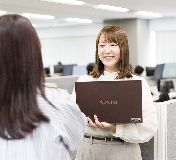 パソコンを持ち同僚と話すH.Aさんの様子
